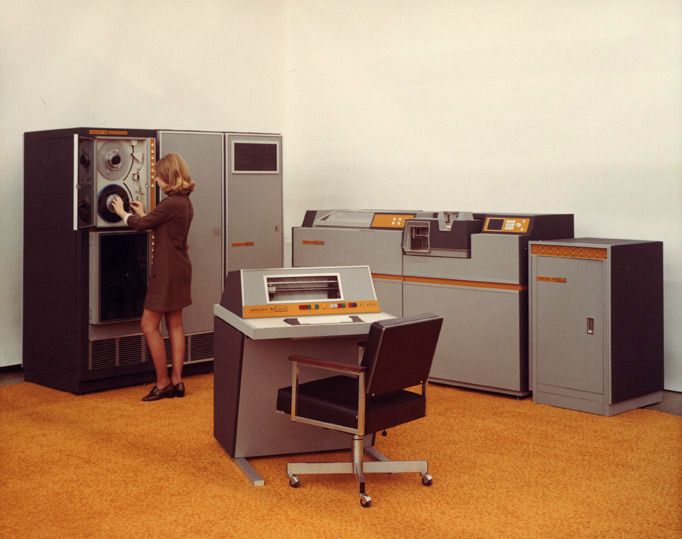 standing woman adjusting tape reel in vintage mainframe computers